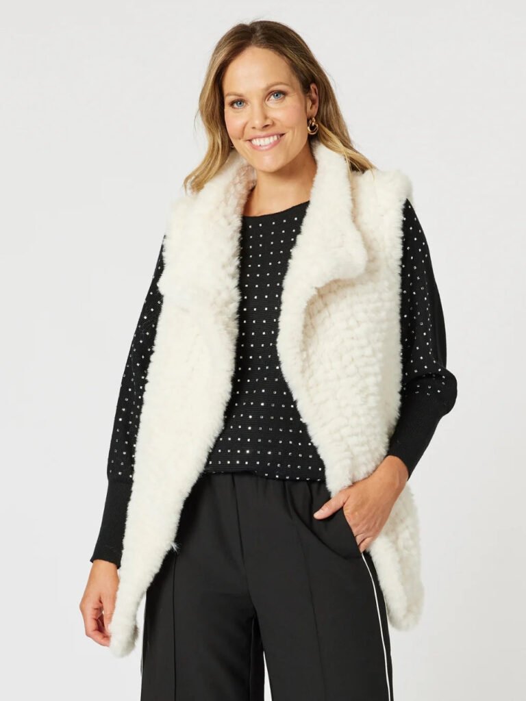 Woman wearing a white fur vest over a black outfit with a white background
