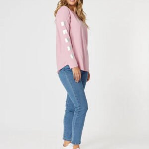 A female model wearing a pink top with heart patterns and blue slim leg jeans.