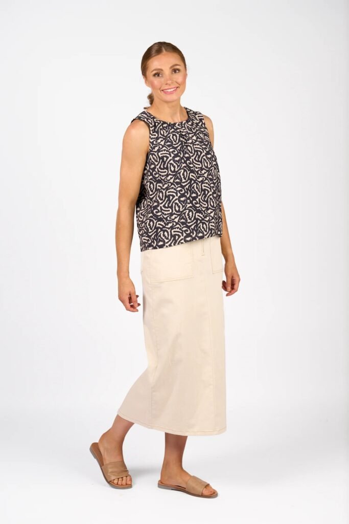 Woman wearing a sleeveless patterned top and beige skirt on a white background