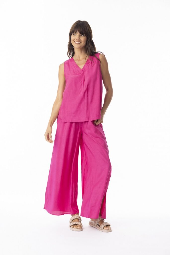 Woman wearing a bright pink sleeveless top and wide-leg pants on a white background